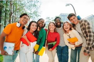 Um grupo de adolescentes sorrindo, segurando pastas e cadernos, posando juntos ao ar livre em um ambiente urbano, transmitindo alegria e diversidade.