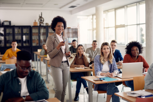 Na imagem, uma professora interage com seus alunos em uma sala de aula, simbolizando a importância do Dia do Professor e o papel crucial dos educadores na formação dos estudantes.