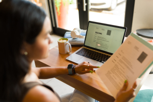 Mulher analisando seu currículo em uma mesa com um laptop aberto e um documento impresso, simbolizando preparação para o mercado de trabalho e o uso do banco de talentos para buscar oportunidades profissionais.