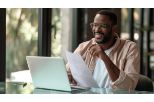 homem negro sorrindo para um computador enquanto manuseia papeis.