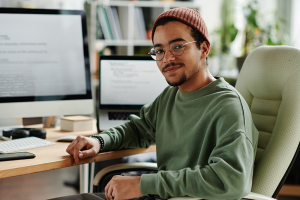 Jovem em frente à uma tela de computador, olhando para a foto e sorrindo. 