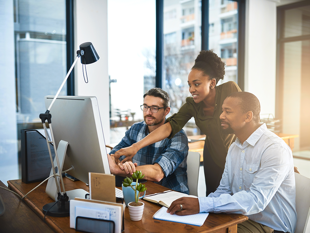 Um grupo de pessoas felizes em frente a uma mesa de trabalho olhando para a tela de um computador.