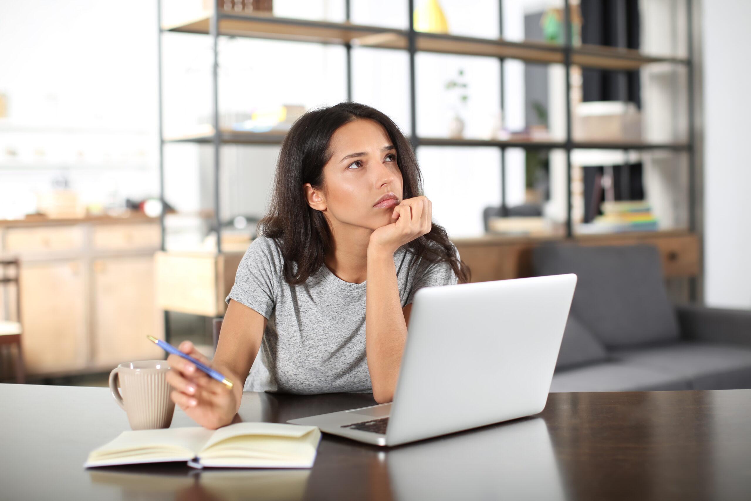 Mulher pensativa com notebook e caneta em uma mesa de escritório, pensando e refletindo sobre ideias ou decisões importantes.