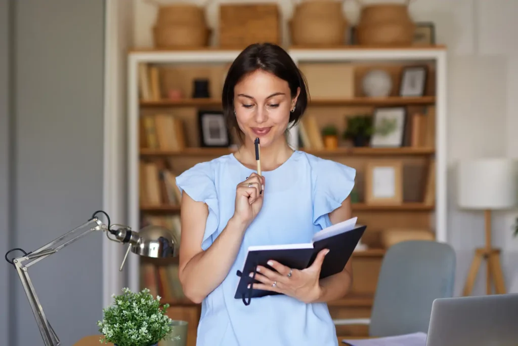Mulher estudando em casa, praticando técnicas para aumentar sua produtividade nos estudos, com um caderno e um celular, em ambiente organizado e acolhedor.
