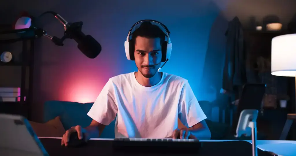 Jovem com headset em frente ao computador, em um quarto com luz neon azul e rosa, ilustrando o curso de games