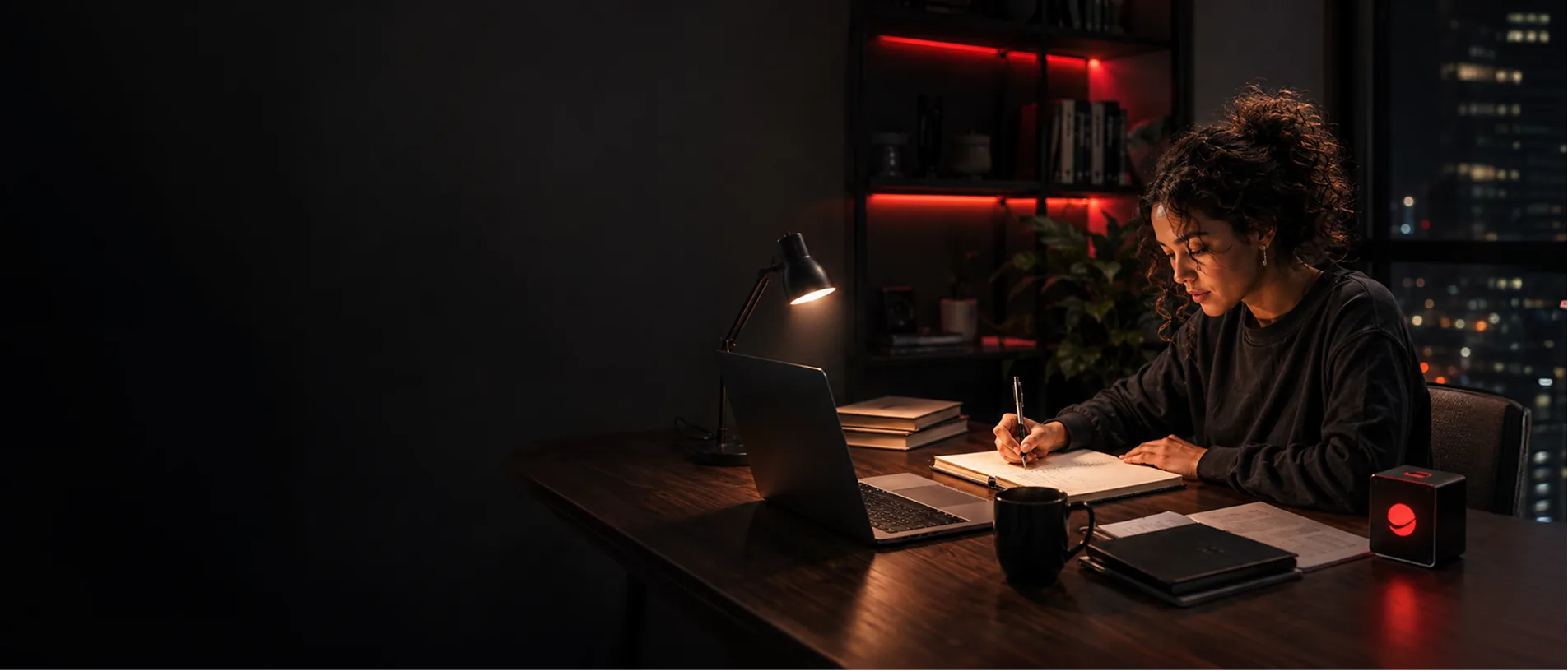 Estudante sentada à mesa de estudos escrevendo no caderno à noite com auxílio de laptop e iluminação aconchegante