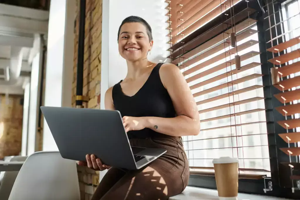 Mulher sorridente usando notebook em escritório moderno — exemplo de profissional aplicando inteligência artificial no trabalho para ganhar produtividade