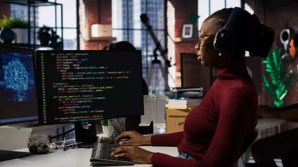 O que é machine learning. Profissional com headset em um escritório, trabalhando em frente a monitores com código de programação.